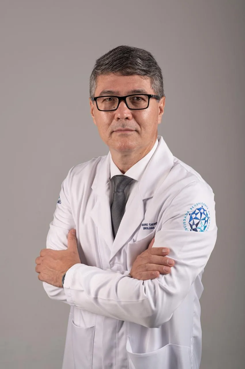 Dr. Nário Takimoto de jaleco branco, braços cruzados, em fundo cinza