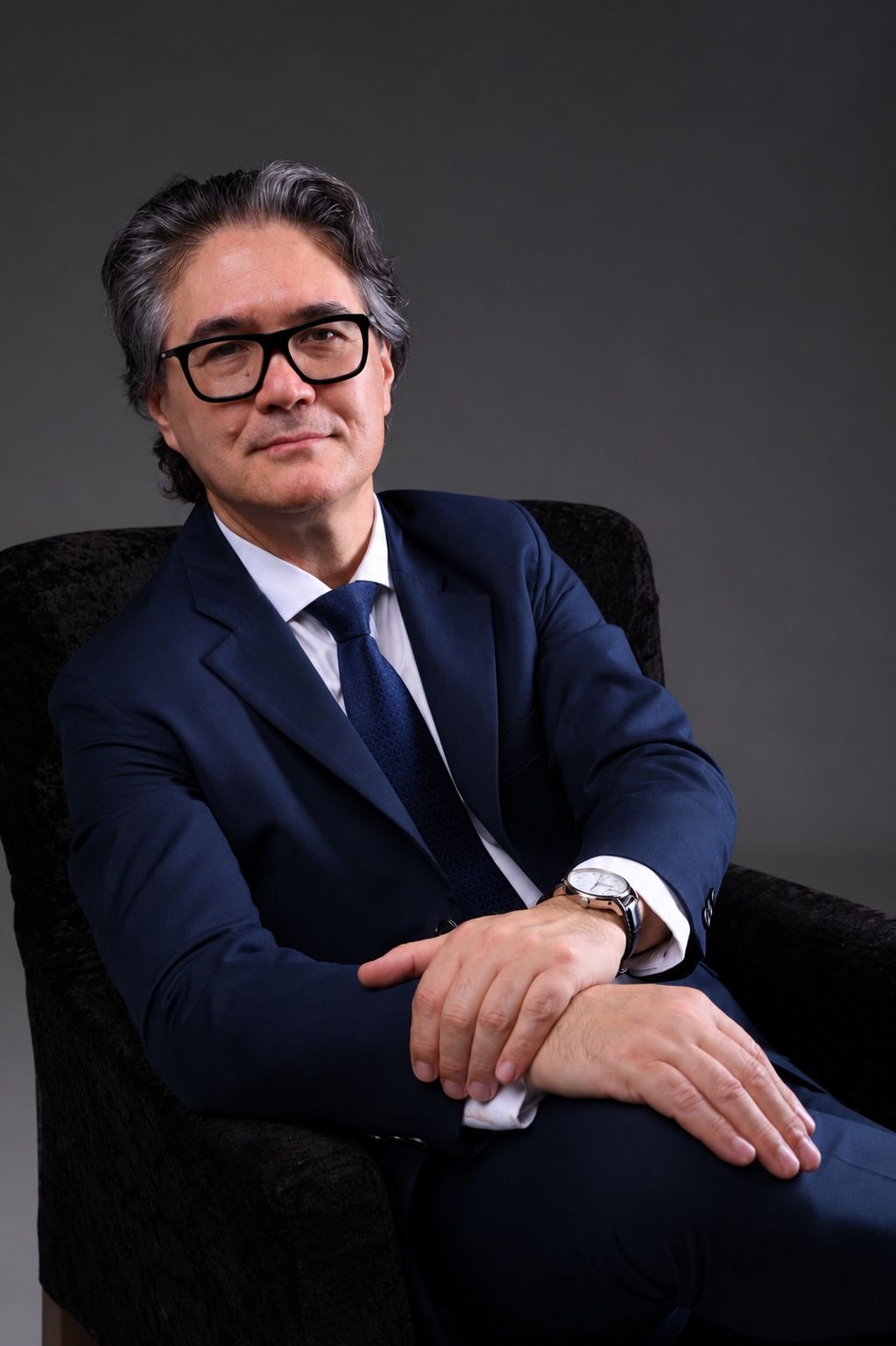 Dr. Nário Takimoto, de terno azul e óculos, sentado em uma poltrona escura